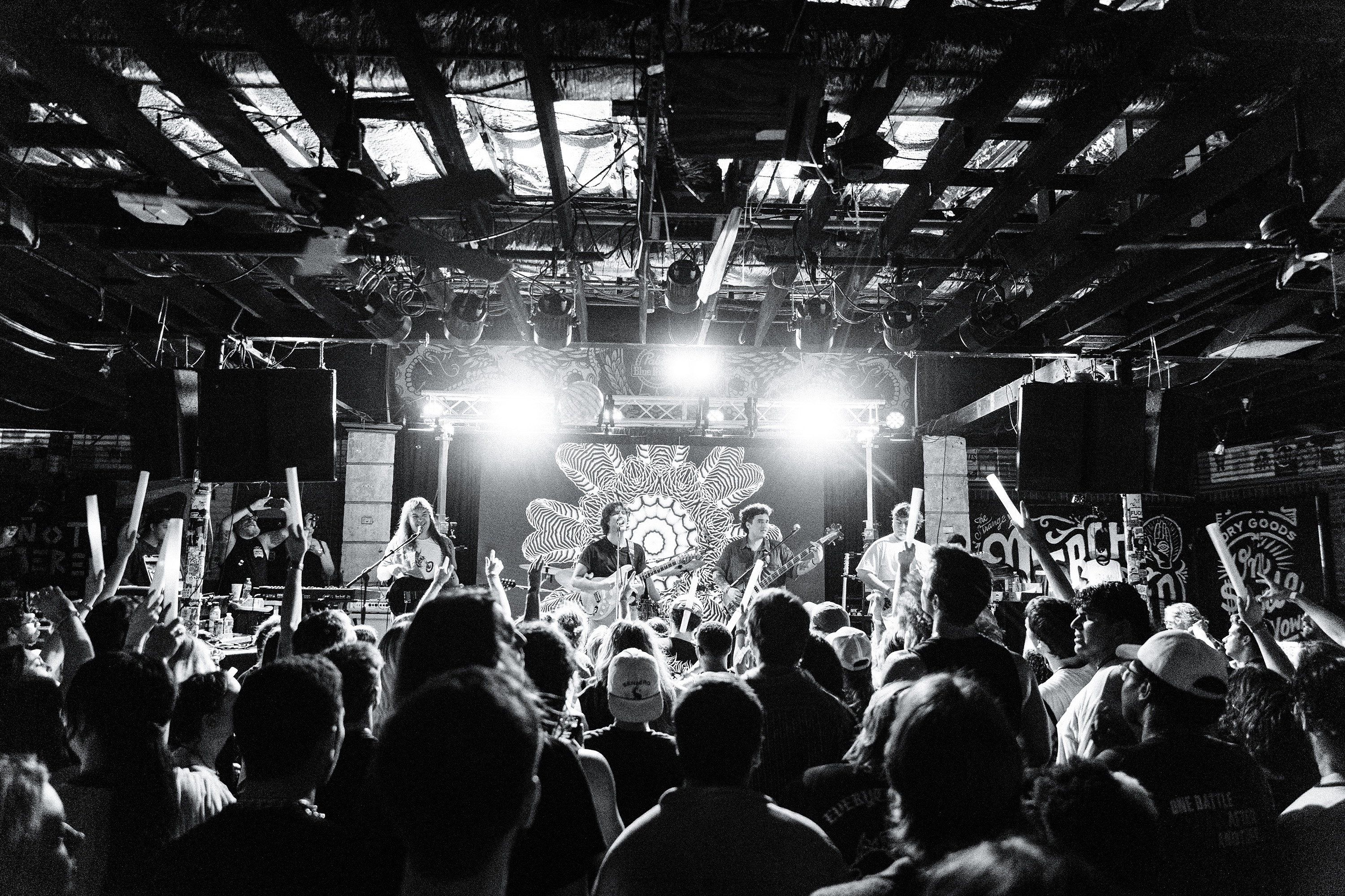 Black and white shot of the crowd, the band is seen performing.
