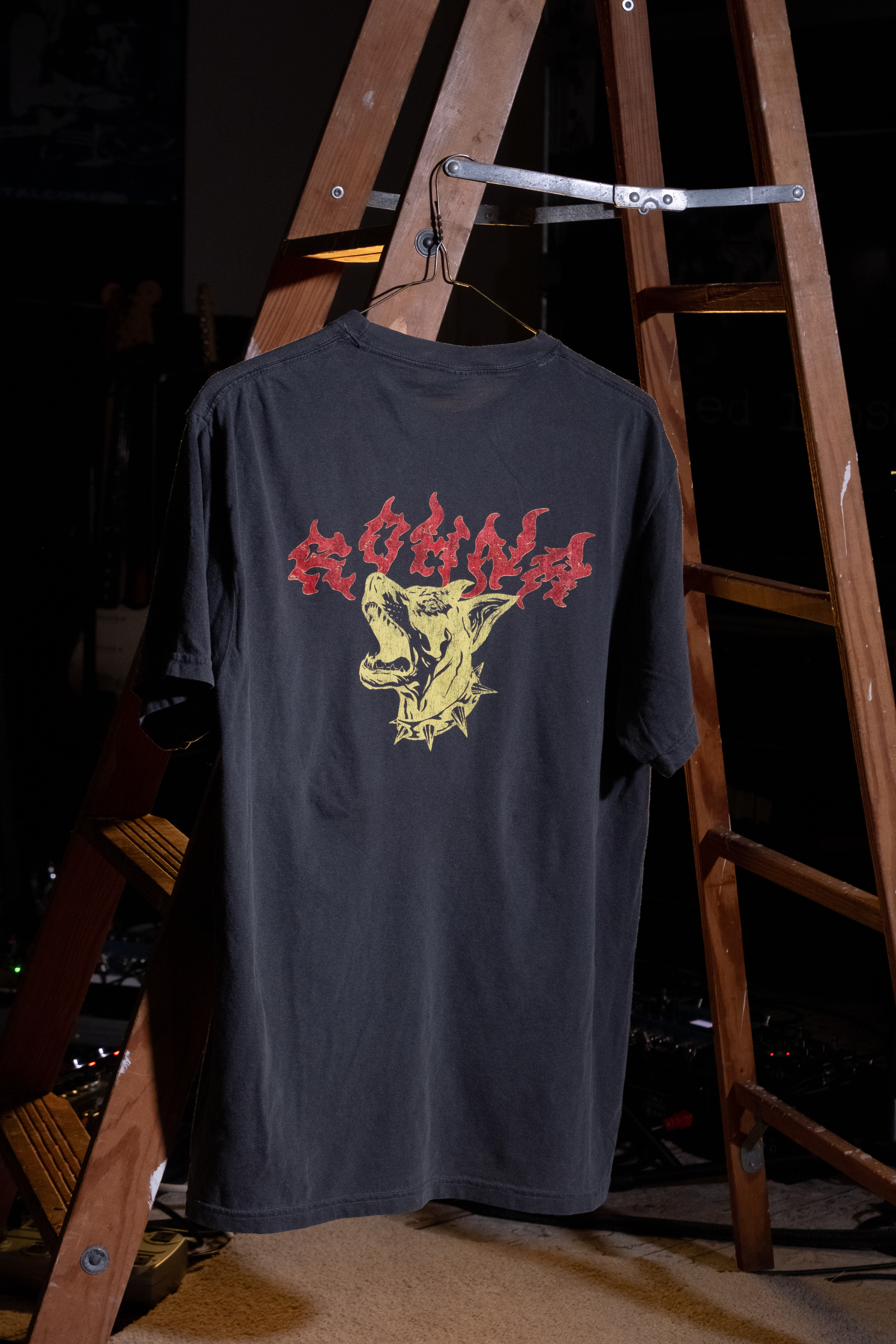 A photo of a band t-shirt on a hanger, suspended from the rung of a wooden ladder.